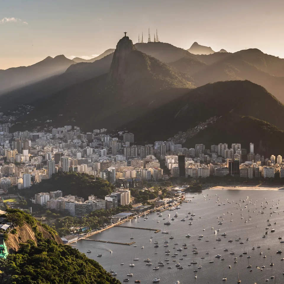 Rio de Janeiro at golden hour: mountains in haze, the city along the bay, and boats moored in the water below
