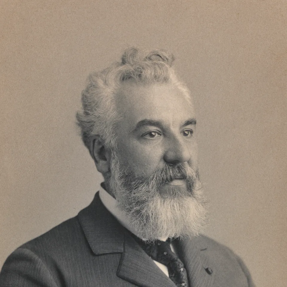 Sepia studio portrait of Alexander Graham Bell, white-bearded, in a dark three-piece suit